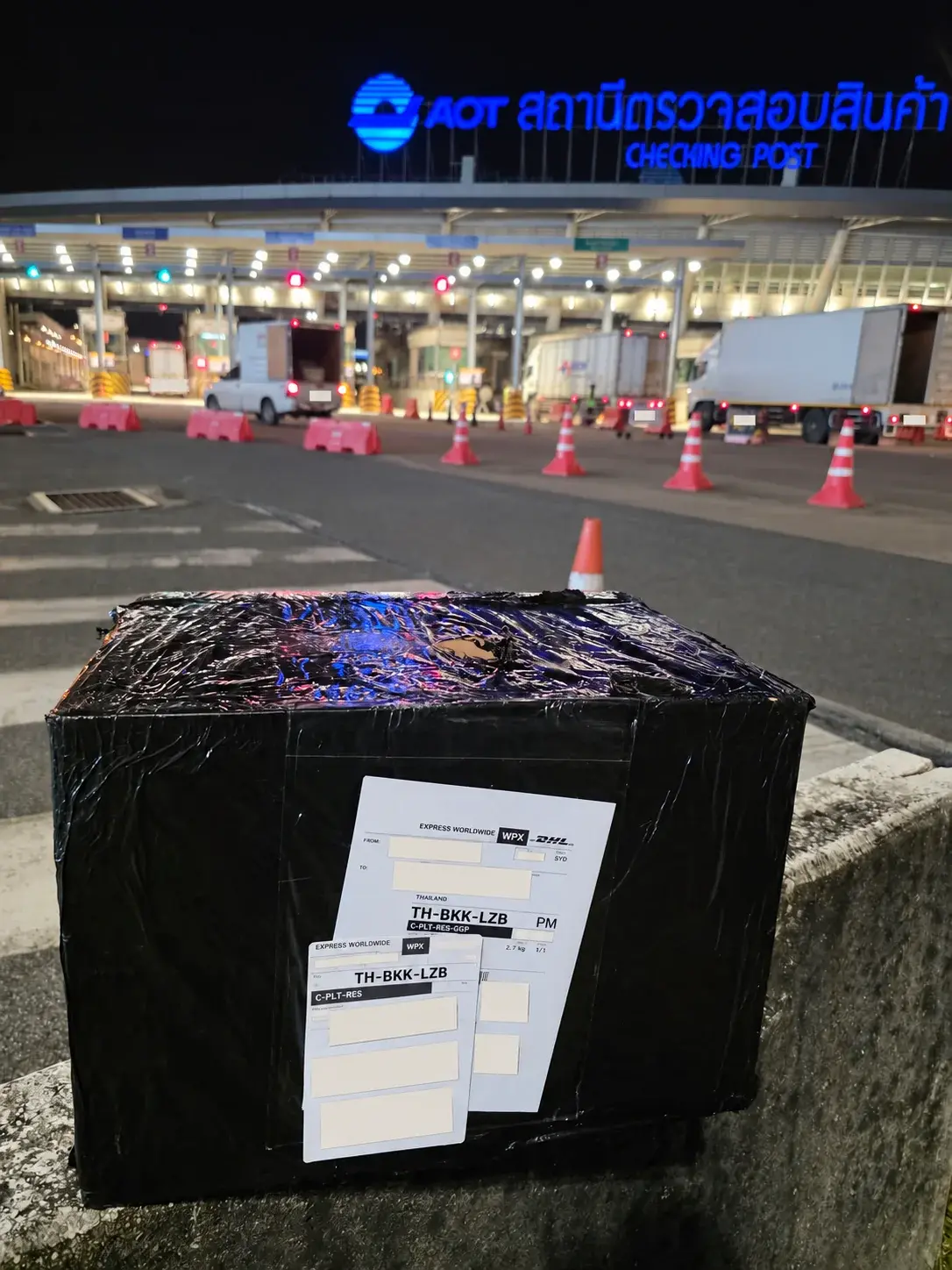 Wrapped parcel outside an AOT cargo checking post at night, with shipping labels concealed